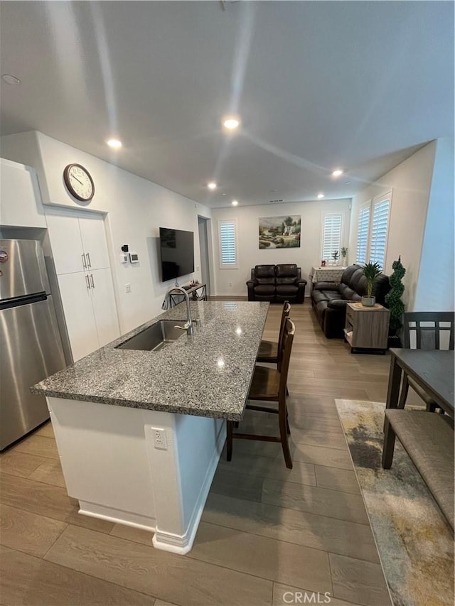 kitchen with freestanding refrigerator, a sink, wood finished floors, white cabinetry, and plenty of natural light