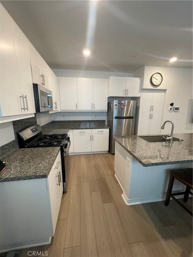kitchen featuring stainless steel appliances, a sink, light wood-style floors, dark stone countertops, and white cabinets