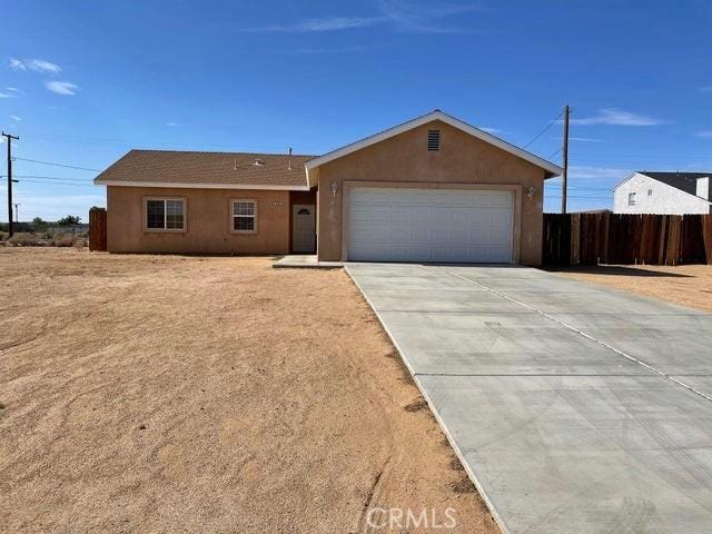 single story home with concrete driveway, stucco siding, fence, and an attached garage