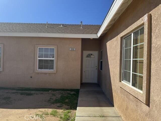 entrance to property featuring stucco siding and roof with shingles