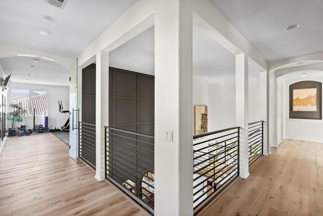 hall with an upstairs landing, arched walkways, and wood finished floors