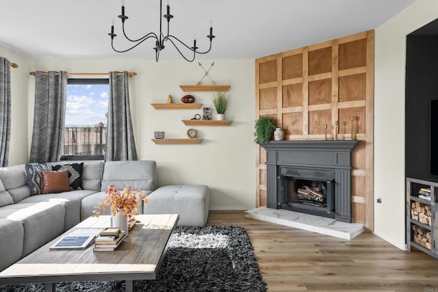 living area featuring baseboards, a fireplace with raised hearth, wood finished floors, and an inviting chandelier