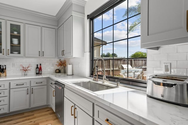 kitchen with gray cabinetry, backsplash, a sink, dishwasher, and light wood-style flooring