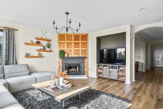 living room with arched walkways, a fireplace with raised hearth, wood finished floors, and an inviting chandelier