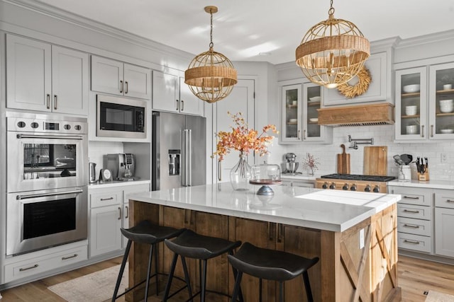 kitchen featuring backsplash, light wood finished floors, stainless steel appliances, a center island, and a notable chandelier
