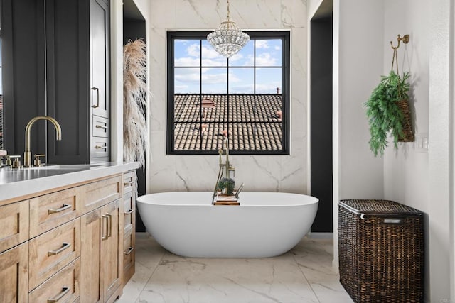 bathroom with marble finish floor, a freestanding tub, vanity, and a chandelier