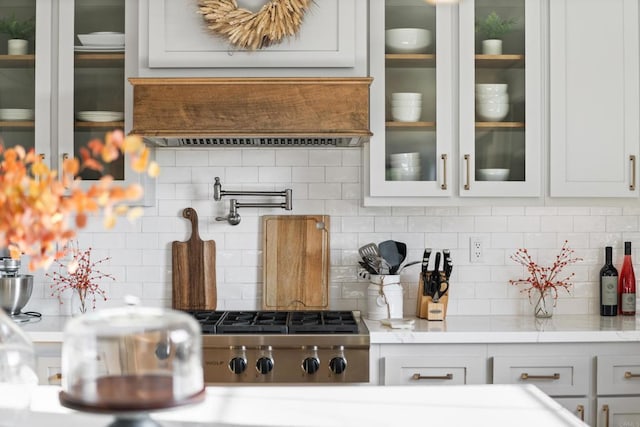 kitchen with decorative backsplash, light countertops, white cabinets, stainless steel gas cooktop, and glass insert cabinets