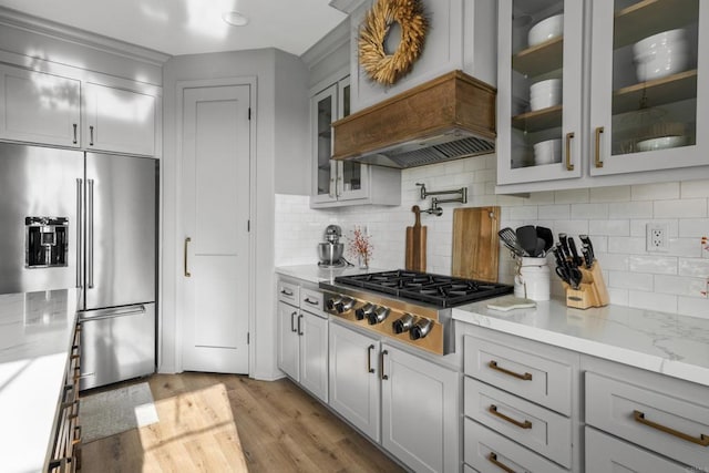 kitchen featuring light stone countertops, backsplash, light wood-type flooring, and appliances with stainless steel finishes
