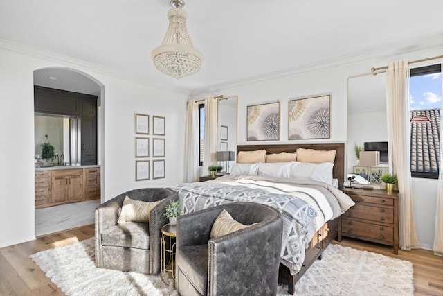 bedroom featuring ornamental molding, a chandelier, arched walkways, connected bathroom, and wood finished floors