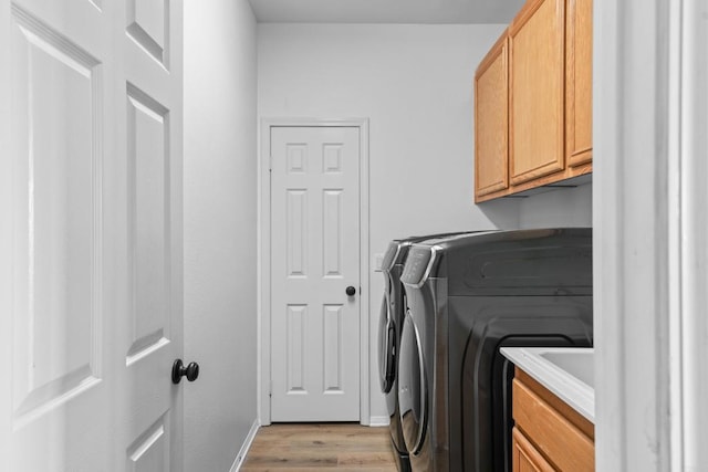 clothes washing area with baseboards, washing machine and dryer, cabinet space, and light wood-type flooring
