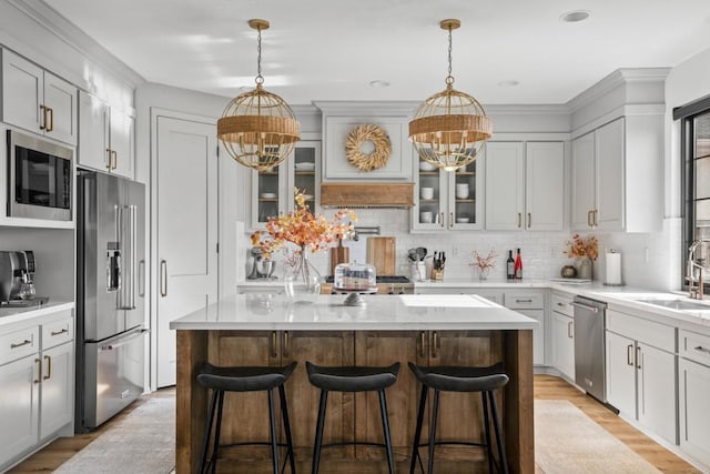 kitchen with a notable chandelier, backsplash, appliances with stainless steel finishes, a center island, and light wood-style floors