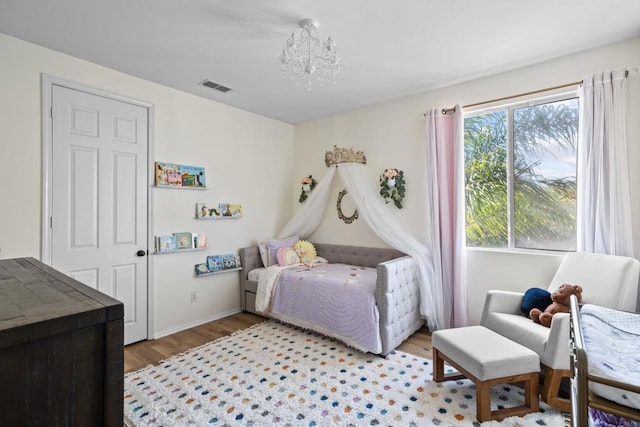 bedroom with baseboards, visible vents, light wood-type flooring, and a chandelier