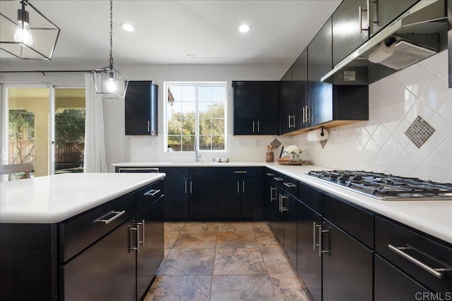 46525 Peach Tree St, Temecula, CA 92592 - kitchen with stainless steel gas cooktop, under cabinet range hood, dark cabinetry, decorative backsplash, and light countertops