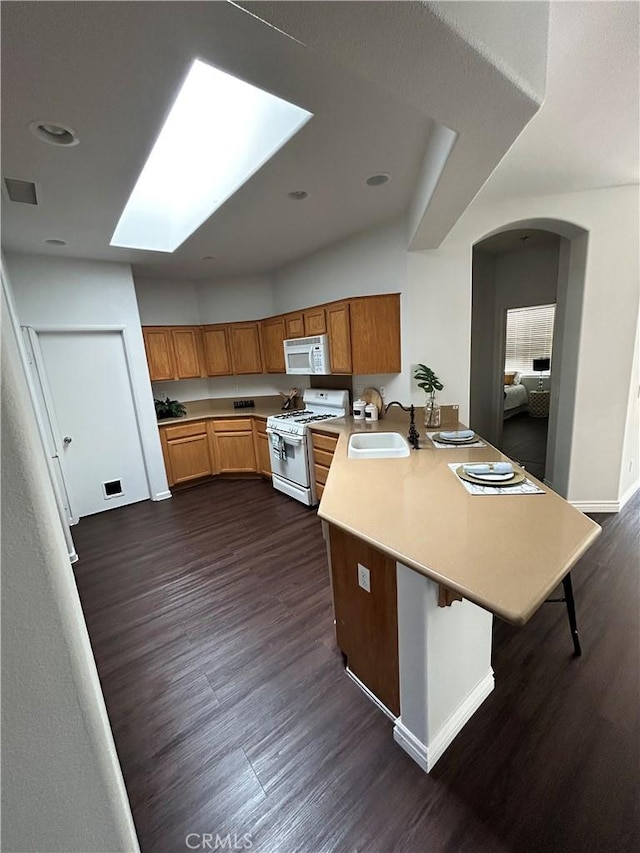 kitchen with light countertops, a peninsula, white appliances, a sink, and dark wood-style floors