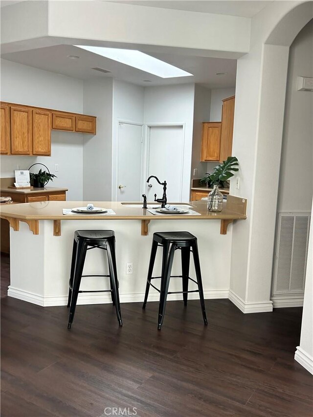 kitchen with a skylight, brown cabinets, dark wood-type flooring, and visible vents