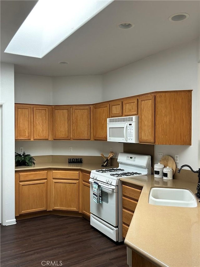 kitchen featuring light countertops, a sink, a skylight, dark wood-style floors, and white appliances