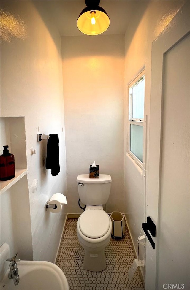 half bath featuring baseboards, a sink, tile patterned floors, and toilet