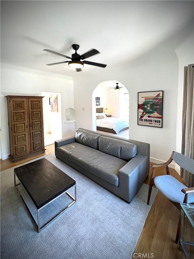 living area featuring a ceiling fan, arched walkways, baseboards, and wood finished floors