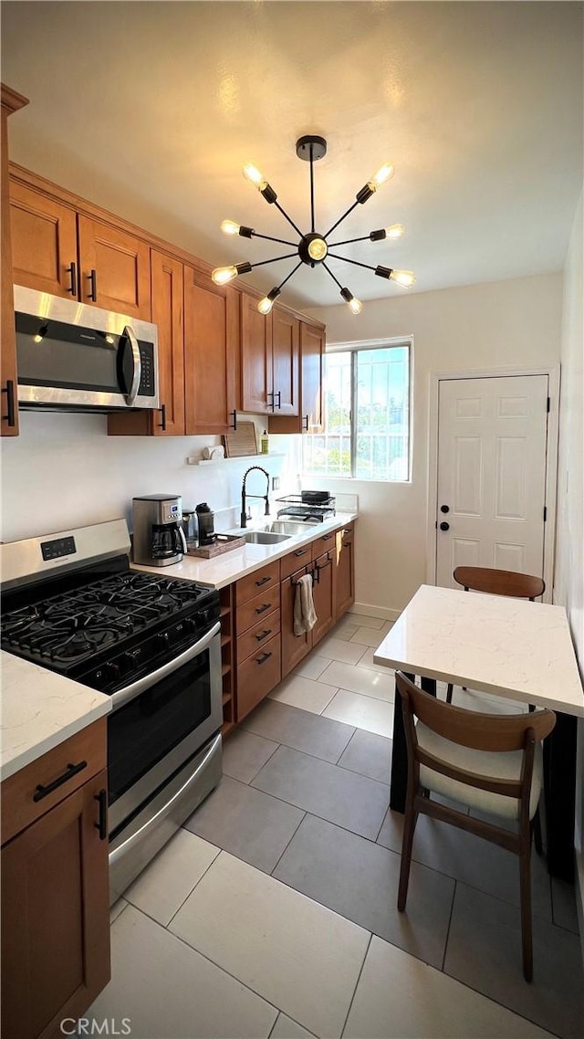kitchen featuring light tile patterned flooring, brown cabinets, appliances with stainless steel finishes, a sink, and a notable chandelier