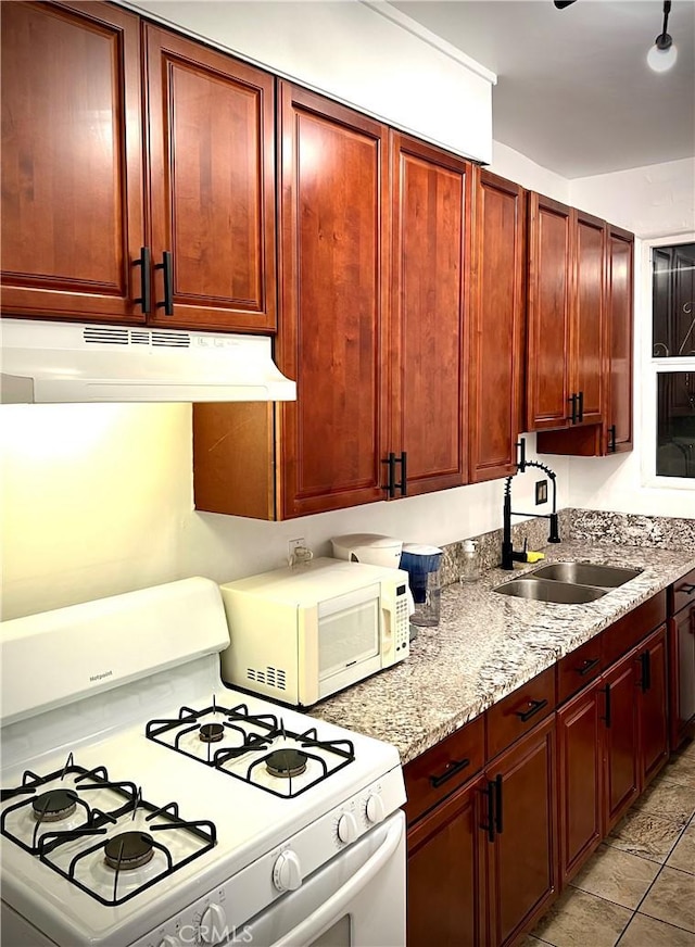 kitchen with white appliances, under cabinet range hood, a sink, reddish brown cabinets, and light stone counters