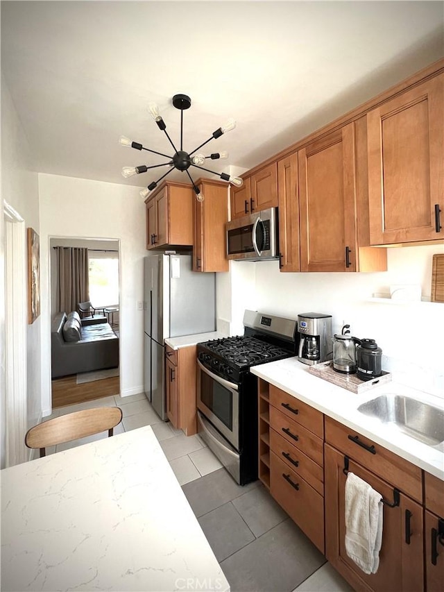 kitchen with light tile patterned flooring, light countertops, stainless steel appliances, an inviting chandelier, and brown cabinetry
