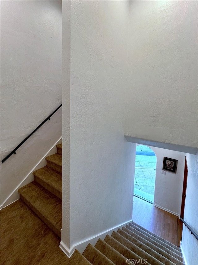 stairs with arched walkways, wood finished floors, and a textured wall
