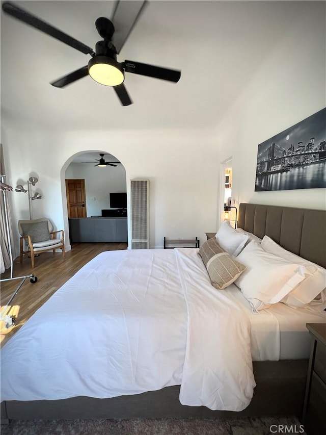 bedroom with arched walkways, wood finished floors, and ceiling fan