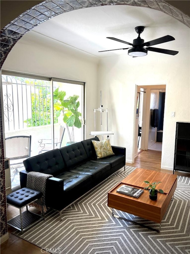 living area featuring baseboards, arched walkways, wood finished floors, and ceiling fan