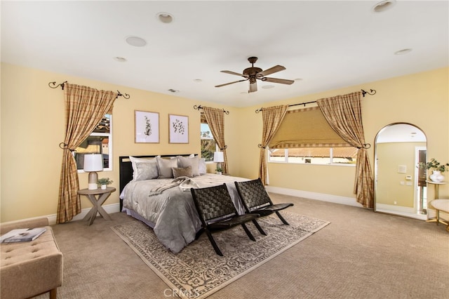 bedroom featuring ceiling fan, baseboards, arched walkways, and light colored carpet