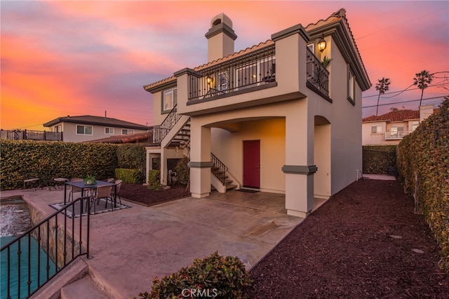 back of property at dusk featuring a patio area, a balcony, a fenced backyard, stucco siding, and stairs