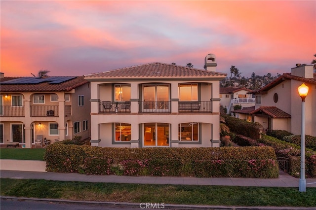 back of property featuring stucco siding, a tile roof, and a balcony