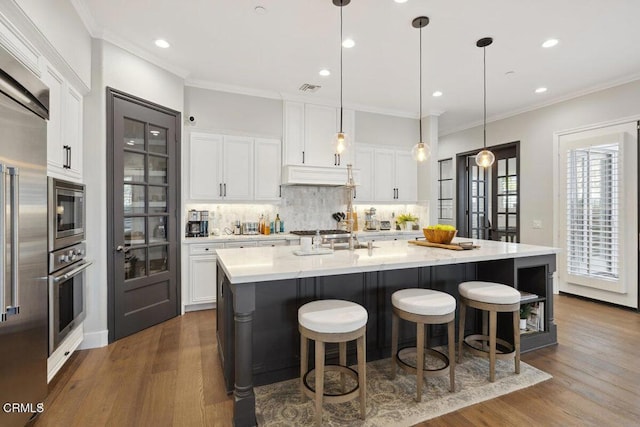 4111 Adriatic St, Oxnard, CA 93035 - kitchen featuring built in appliances, dark wood-type flooring, backsplash, white cabinets, and a breakfast bar area