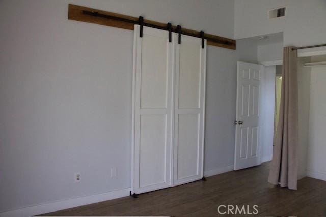 unfurnished bedroom featuring a barn door, visible vents, baseboards, and wood finished floors