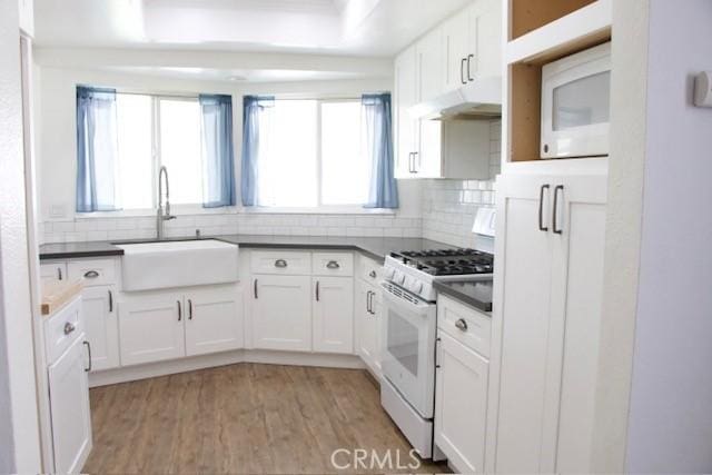 kitchen featuring tasteful backsplash, white appliances, dark countertops, white cabinets, and a sink