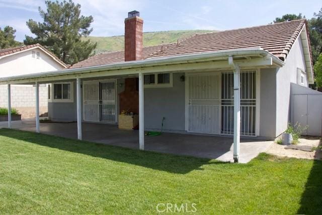 rear view of property with a yard, stucco siding, a patio, and a chimney