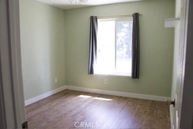 empty room featuring a wealth of natural light, wood finished floors, and baseboards