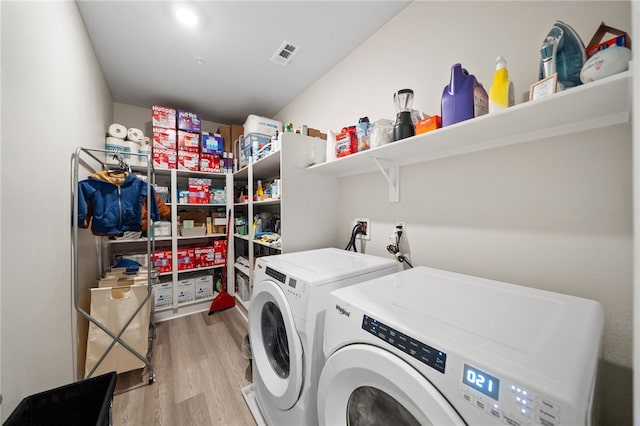 clothes washing area with laundry area, washing machine and dryer, light wood finished floors, and visible vents