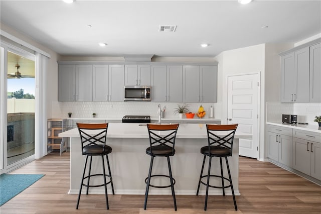 kitchen with appliances with stainless steel finishes, gray cabinets, a kitchen island with sink, and tasteful backsplash