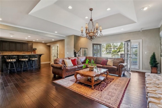 living room with a notable chandelier, a raised ceiling, dark wood-type flooring, baseboards, and indoor bar