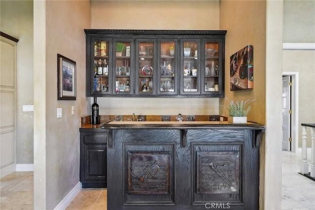 bar featuring baseboards, light tile patterned floors, and indoor wet bar