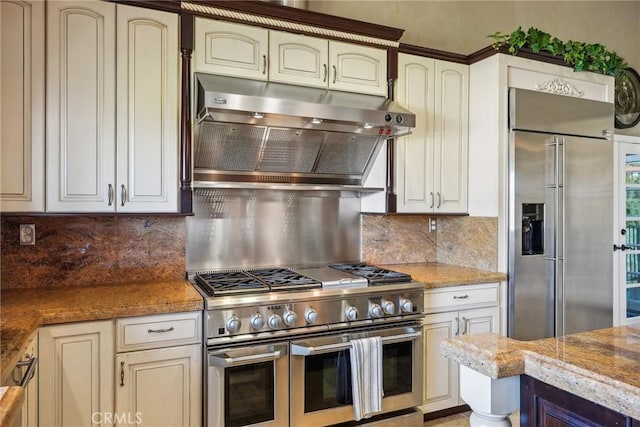 kitchen featuring light stone counters, high end appliances, decorative backsplash, and under cabinet range hood