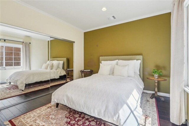 bedroom with wood finished floors, a closet, ornamental molding, baseboards, and visible vents