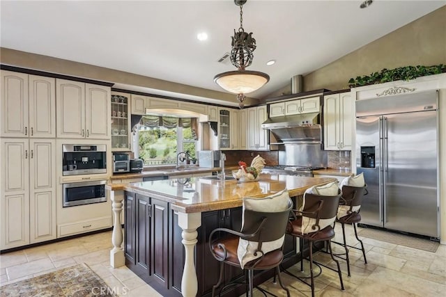 kitchen with stone tile floors, vaulted ceiling, backsplash, and built in fridge