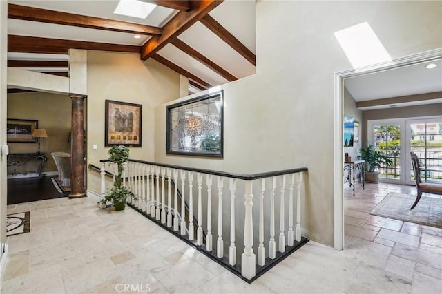 hallway featuring beamed ceiling, stone tile flooring, an upstairs landing, high vaulted ceiling, and a skylight