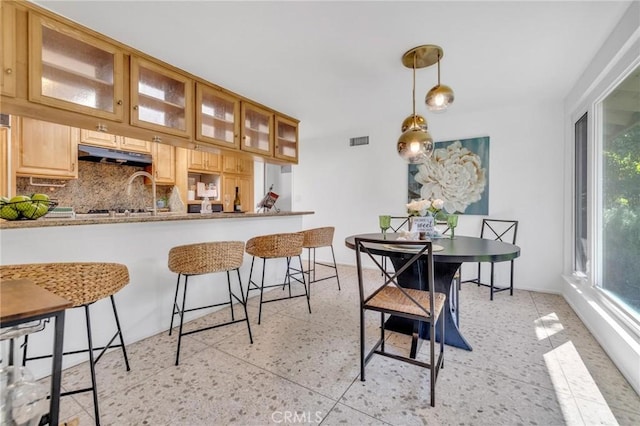 2001 Hacienda Rd, La Habra Heights, CA 90631 - kitchen with under cabinet range hood, a breakfast bar area, tasteful backsplash, glass insert cabinets, and pendant lighting