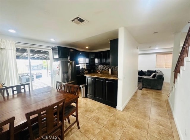 kitchen with light tile patterned flooring, stainless steel fridge with ice dispenser, dark cabinets, tasteful backsplash, and visible vents
