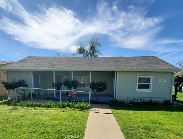 view of front of home featuring roof with shingles, covered porch, and a front yard