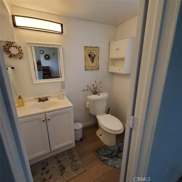 bathroom with toilet, wood finished floors, vanity, and baseboards