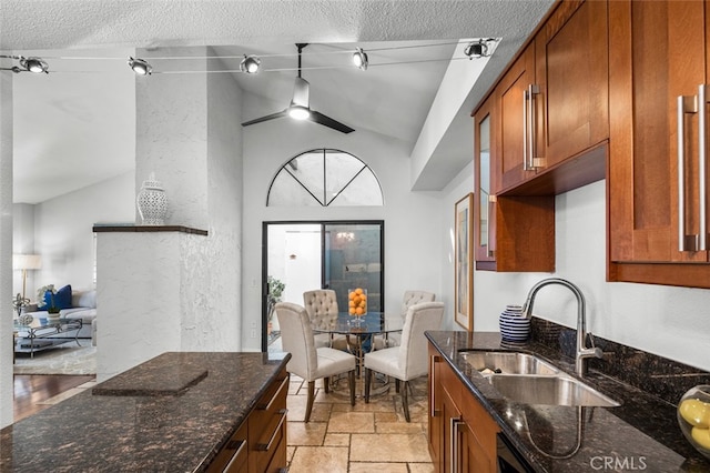 kitchen with vaulted ceiling, dark stone counters, brown cabinetry, and a sink