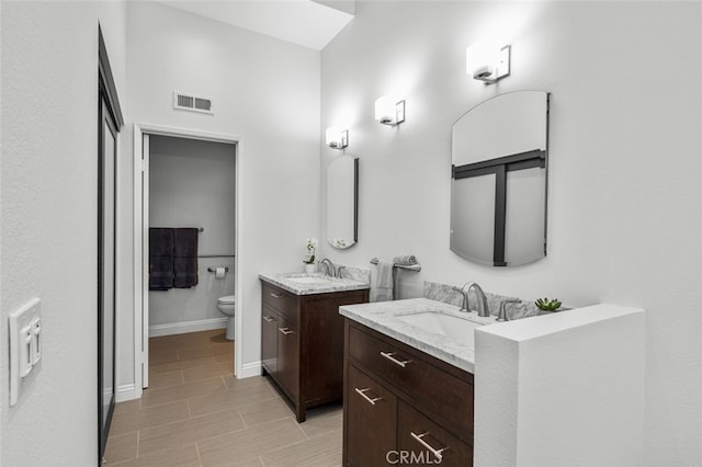 bathroom featuring visible vents, toilet, a sink, baseboards, and two vanities